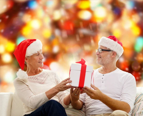 Felice coppia di anziani in cappelli di Babbo Natale con scatola regalo — Foto Stock