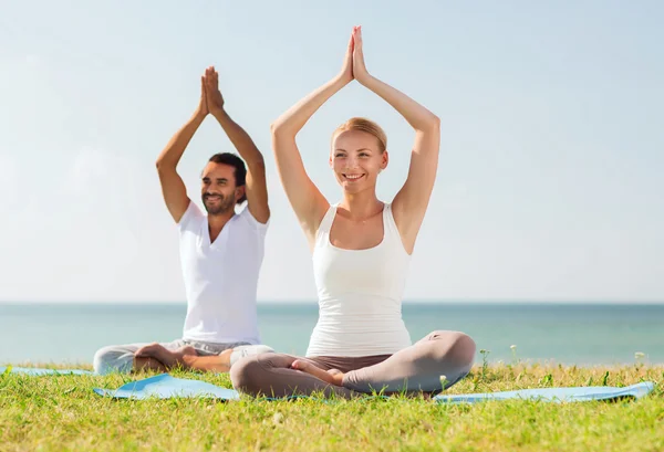 Pareja sonriente haciendo ejercicios de yoga al aire libre —  Fotos de Stock