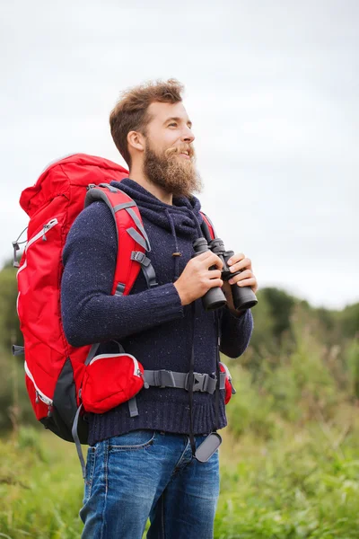 Uomo sorridente con zaino e binocolo all'aperto — Foto Stock