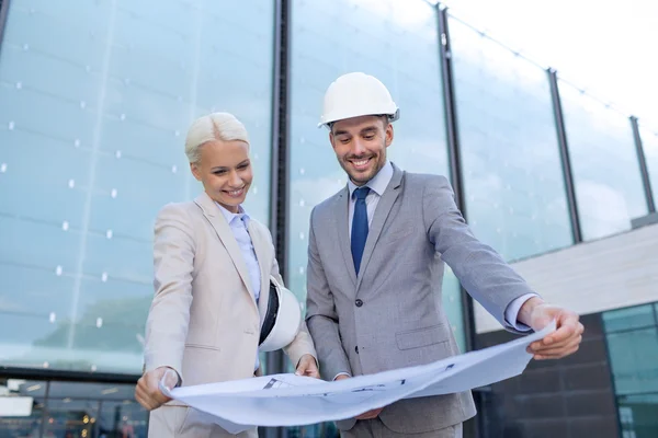 Hombres de negocios sonrientes con planos y cascos — Foto de Stock