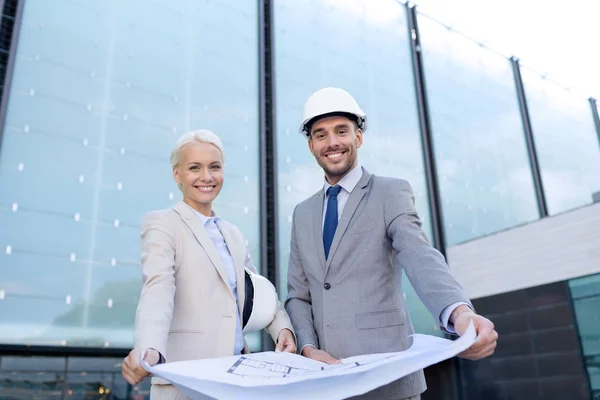 Hombres de negocios sonrientes con planos y cascos — Foto de Stock