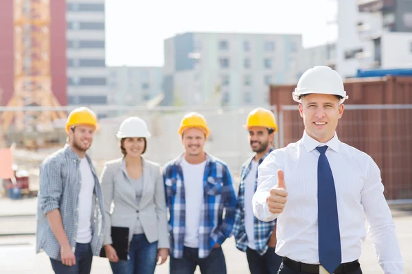 Grupp av leende byggare i hardhats utomhus — Stockfoto