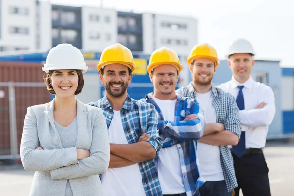 Группа улыбающихся строителей в касках на открытом воздухе — стоковое фото