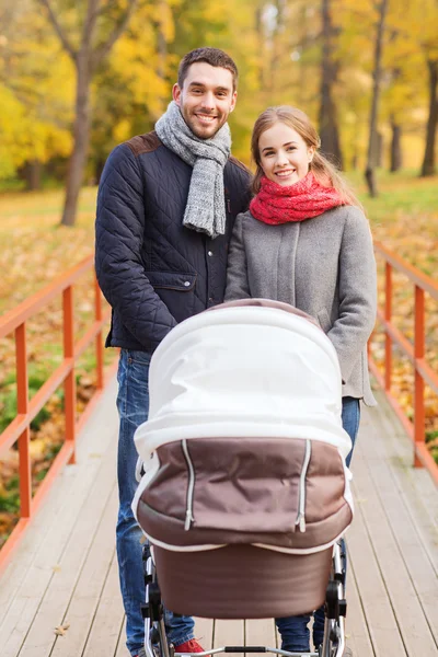 Smiling couple with baby pram in autumn park — Stock Photo, Image