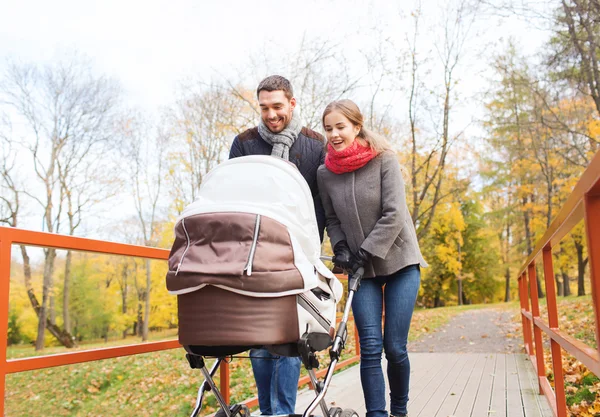 Smiling couple with baby pram in autumn park — Stock Photo, Image