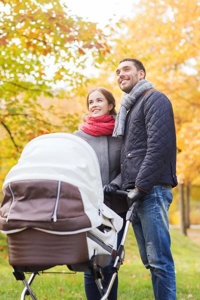 Pareja sonriente con cochecito de bebé en el parque de otoño —  Fotos de Stock