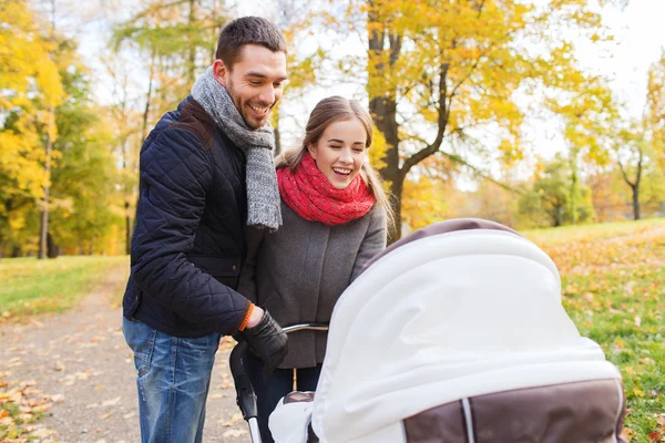 Pareja sonriente con cochecito de bebé en el parque de otoño —  Fotos de Stock