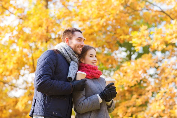 Pareja sonriente con tazas de café en el parque de otoño —  Fotos de Stock