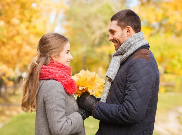 Pareja sonriente con racimo de hojas en el parque de otoño — Foto de Stock