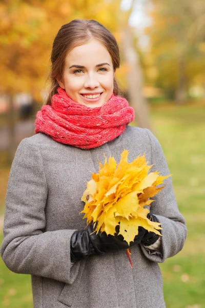 Mulher sorridente com cacho de folhas no parque de outono — Fotografia de Stock