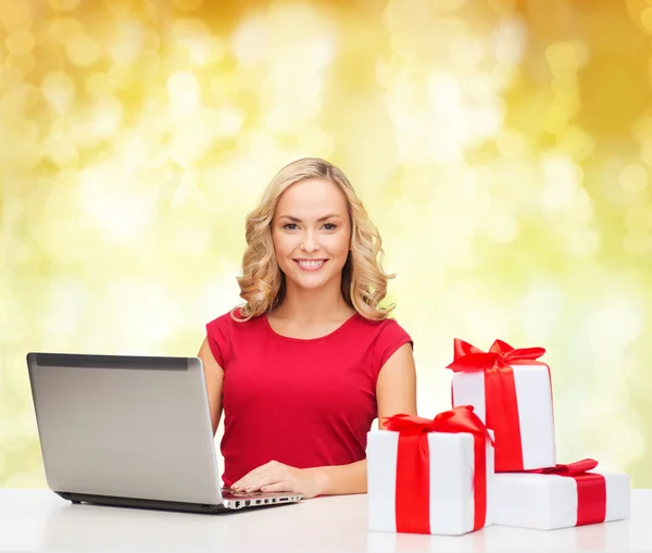 Smiling woman in red shirt with gifts and laptop — Stock Photo, Image