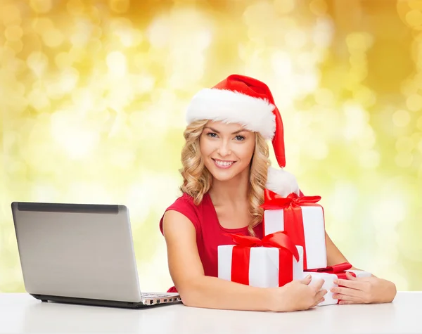 Lachende vrouw in Kerstman hoed met giften en laptop — Stockfoto