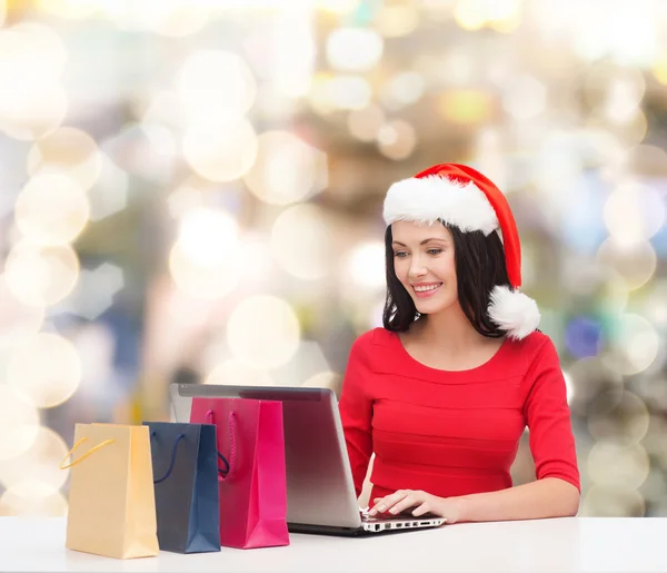 Lachende vrouw in kerstmuts met tassen en laptop — Stockfoto