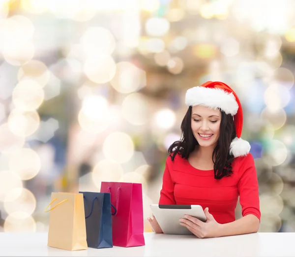 Donna sorridente in cappello di Babbo Natale con borse e tablet pc — Foto Stock