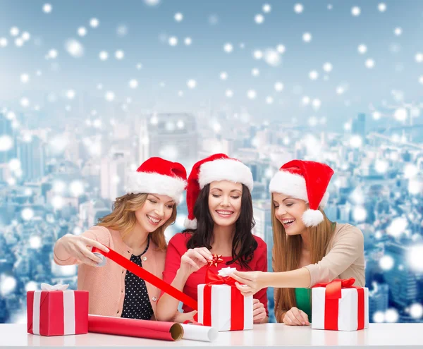 Donne sorridenti in cappelli Babbo Natale helper imballaggio regali — Foto Stock