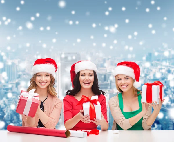 Donne sorridenti in cappelli Babbo Natale helper imballaggio regali — Foto Stock