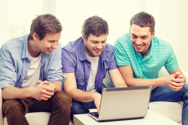 Amigos sonrientes con ordenador portátil en casa —  Fotos de Stock