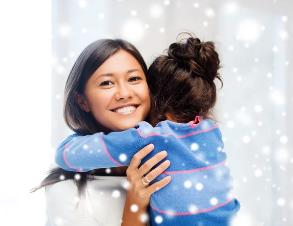 Smiling little girl and mother hugging indoors — Stock Photo, Image