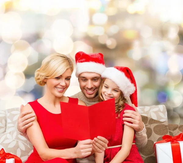 Ευτυχισμένη οικογένεια σε καπέλα santa με ευχετήρια κάρτα — Φωτογραφία Αρχείου
