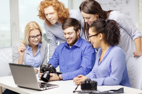 Lächelndes Team mit Laptop und Fotokamera im Büro — Stockfoto