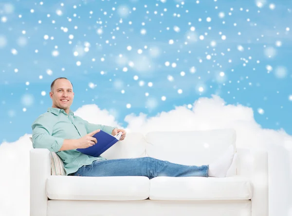 Sorrindo homem com livro deitado no sofá — Fotografia de Stock