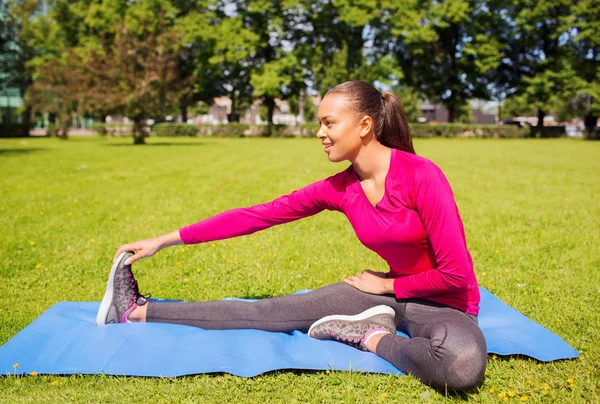 Lächelnde Frau streckt Bein auf Matte im Freien — Stockfoto