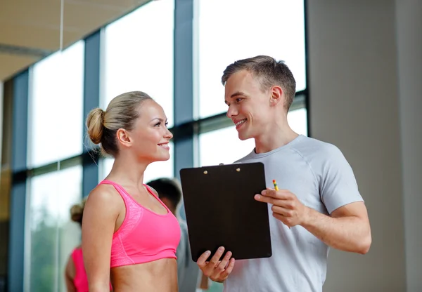 Giovane donna sorridente con personal trainer in palestra — Foto Stock