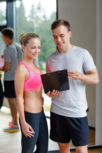 Giovane donna sorridente con personal trainer in palestra — Foto Stock