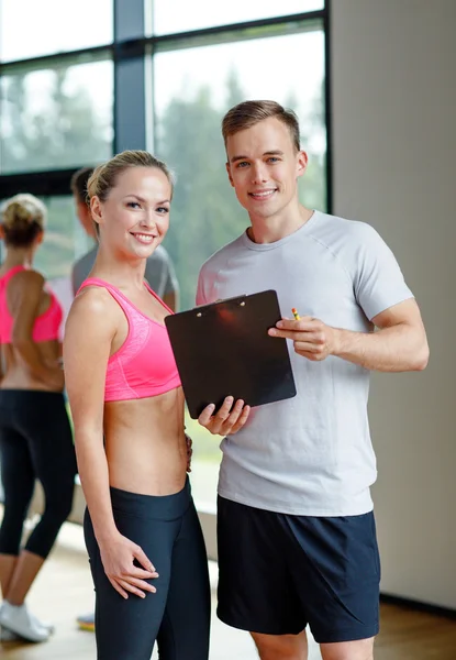 Sorrindo jovem mulher com personal trainer no ginásio — Fotografia de Stock