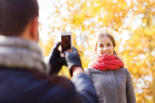Smiling couple with smartphone in autumn park — Stock Photo, Image