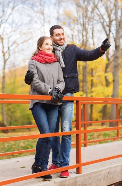 Coppia sorridente che si abbraccia sul ponte nel parco autunnale — Foto Stock