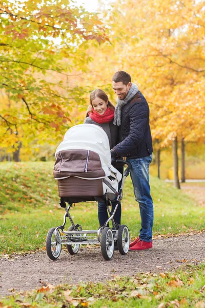 Улыбающаяся пара с детской коляской в осеннем парке — стоковое фото
