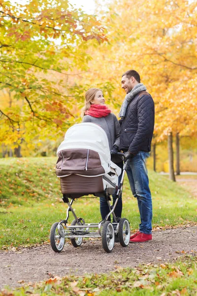 Smiling couple with baby pram in autumn park — Stock Photo, Image