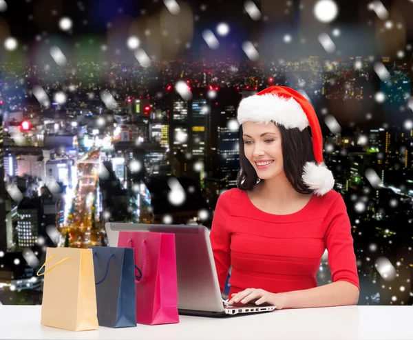 Donna sorridente in cappello di Babbo Natale con borse e laptop — Foto Stock