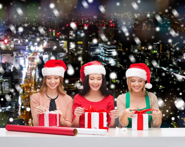 Donne sorridenti in cappelli Babbo Natale helper imballaggio regali — Foto Stock