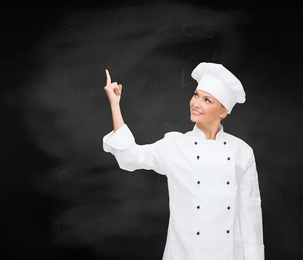Chef sorridente do sexo feminino apontando dedo para algo — Fotografia de Stock