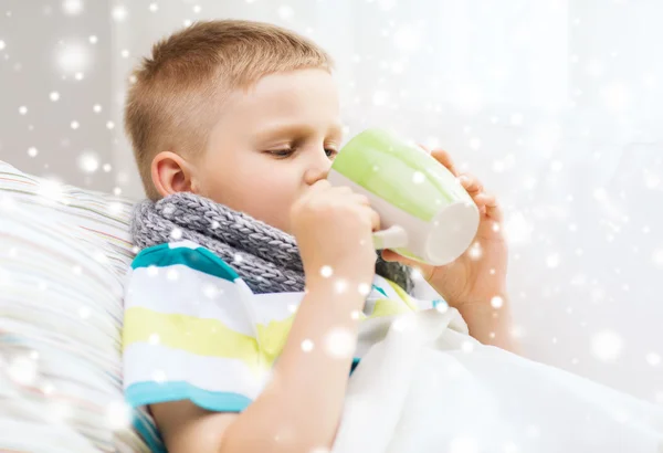 Больной мальчик с гриппом в постели пьет из чашки дома — стоковое фото