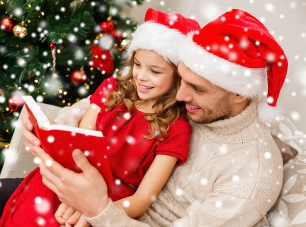Lächelnder Vater und Mädchen mit Weihnachtsmannhüten lesen Buch — Stockfoto