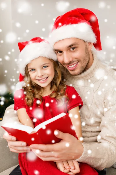 Sonriente padre y chica en los sombreros de santa lectura libro — Foto de Stock
