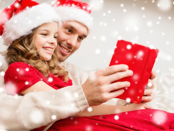 Lachende vader en meisje in santa hoeden lezen van boek — Stockfoto
