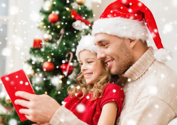 Souriant père et fille dans santa chapeaux lecture livre — Photo