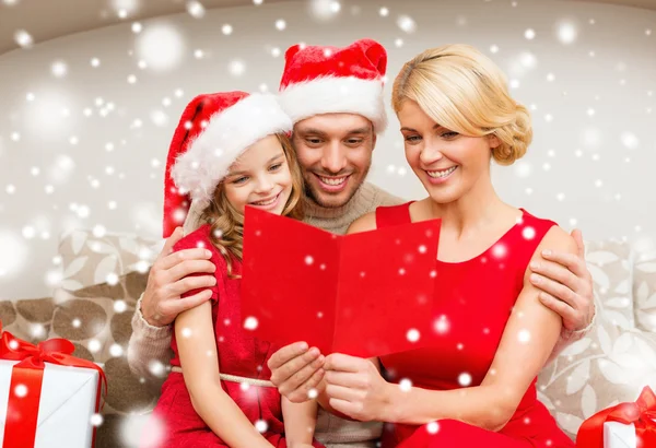 Famille souriante dans santa chapeaux lecture carte postale — Photo