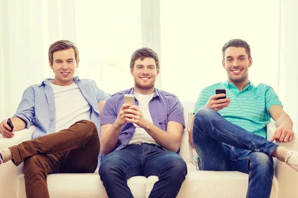 Amici sorridenti con gli smartphone a casa — Foto Stock