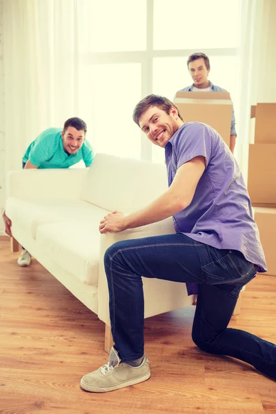 Smiling friends with sofa and boxes at new home — Stock Photo, Image