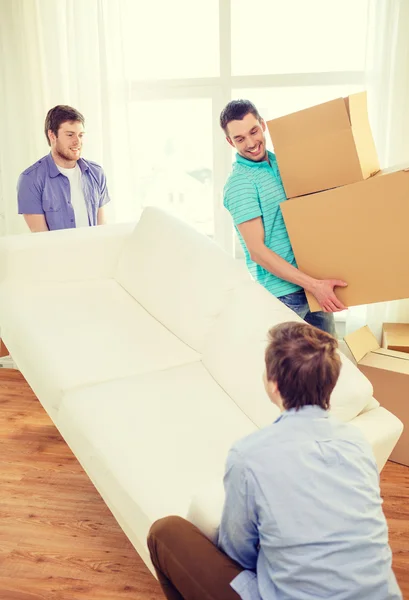 Smiling friends with sofa and boxes at new home — Stock Photo, Image