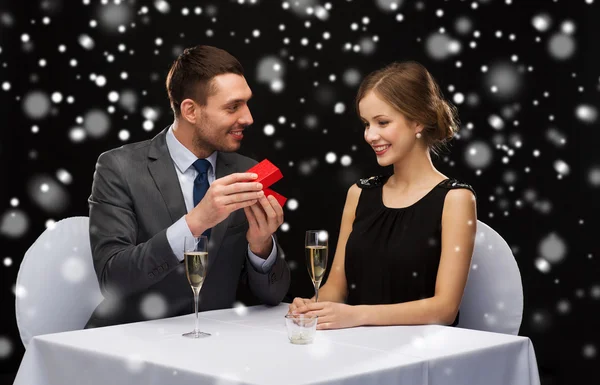 Casal sorridente com caixa de presente vermelho no restaurante — Fotografia de Stock