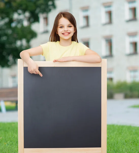 Happy little girl pointing finger to blackboard — Stock Photo, Image