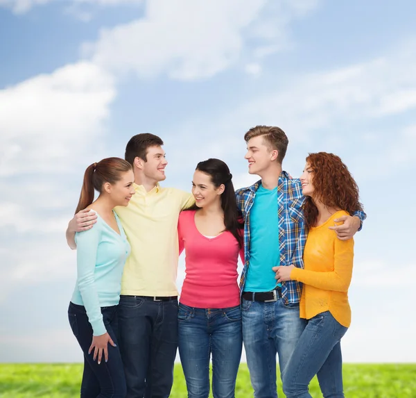 Группа улыбающихся подростков над голубым небом и травой — стоковое фото