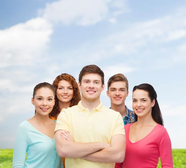 Group of smiling teenagers over blue sky and grass — Stock Photo, Image