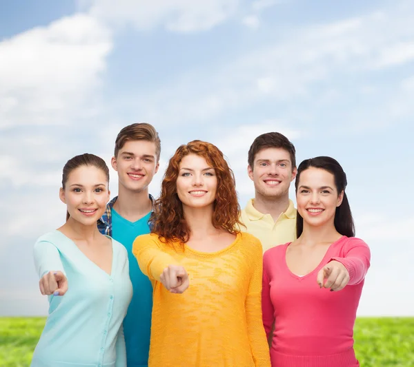 Group of smiling teenagers over blue sky and grass — Stock Photo, Image